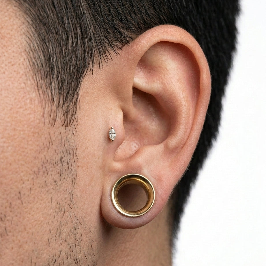 Close-up of an ear with a small marquise gold piercing earring