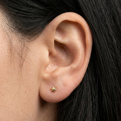Close-up of an ear wearing a gold star-shaped stud earring with dark hair.